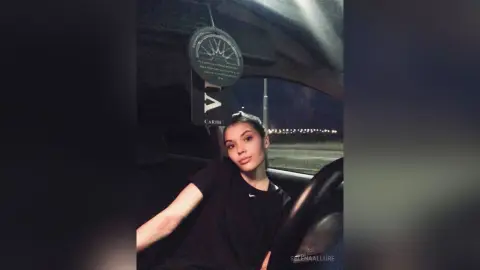 Young woman in a black t-shirt sitting in a car at night with a moody, cinematic atmosphere.