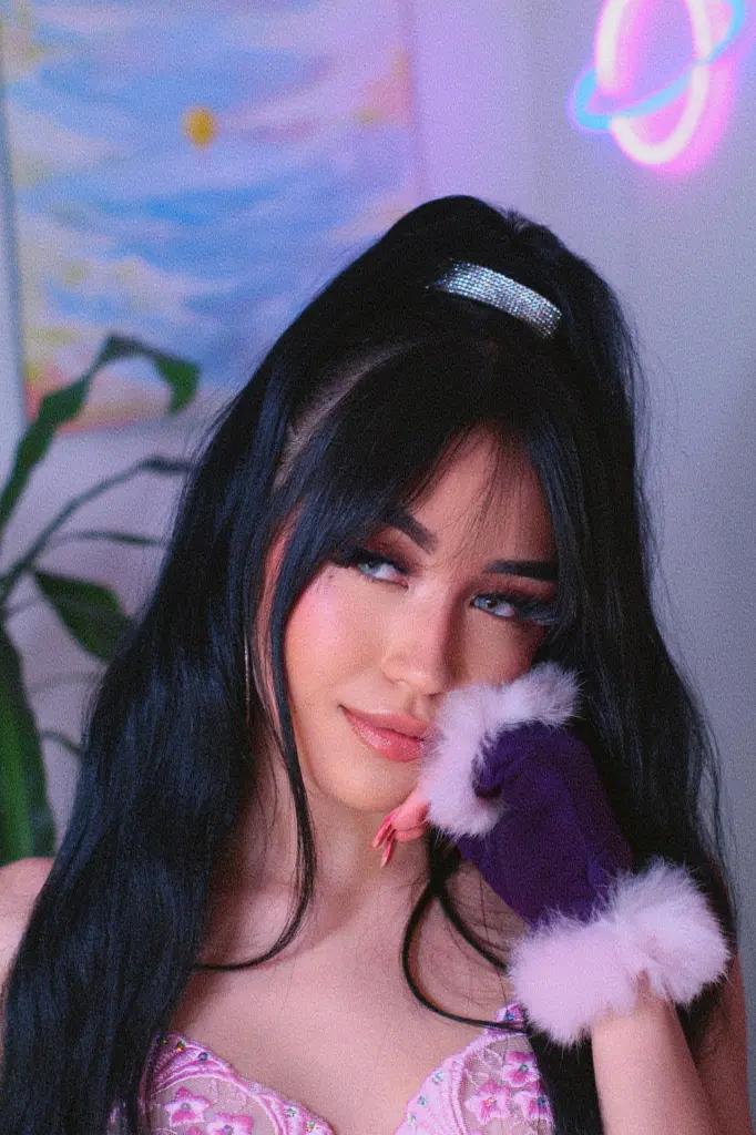 ThaliaZafirr — Young woman with long dark hair and pink lace top posing in a dreamy, neon-lit room.