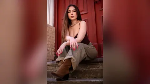 Stylish woman in a dark tank top and olive trousers sitting on stone steps by a red door.
