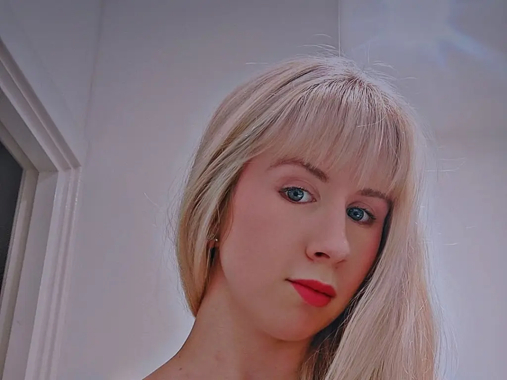 Lilybee24 looks directly at the camera with blonde hair and red lipstick against a plain white background.