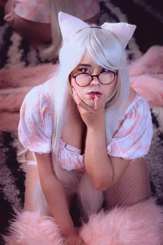 Girl in pink cosplay outfit and cat ears sitting on pink faux fur in a dreamy aesthetic mood.
