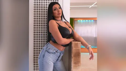 Confident woman in a black crop top and light blue jeans leaning against a pillar in a modern indoor setting.