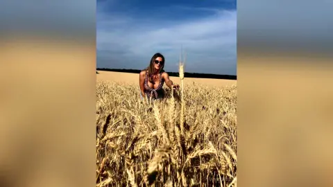 Stylish woman in a patterned romper relaxing in a golden wheat field under a bright blue sky.