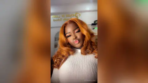 Cheerful woman with long wavy ginger hair wearing a white ribbed turtleneck in a bright indoor setting.