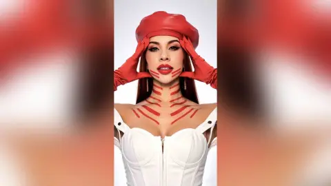 Glamorous woman in a white corset and red beret with artistic red face and body paint against a white background.