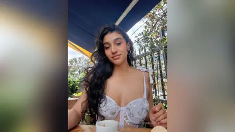 Young woman in a white lace corset top relaxing at an outdoor cafe on a sunny day.
