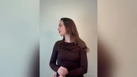 Elegant woman in a dark brown long-sleeve top looking away in a minimalist indoor setting.