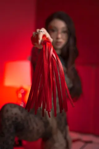 Young woman in a leopard print outfit holding red leather tassels in a moody, red-lit room.