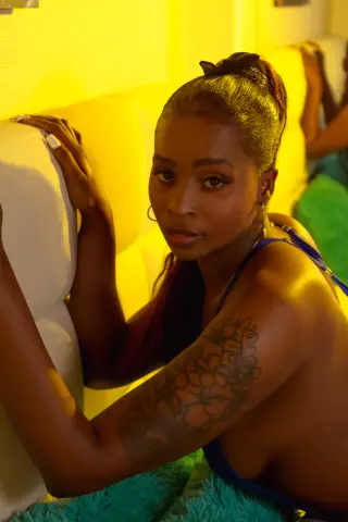 Beautiful Black woman in a blue outfit relaxing on a white sofa under warm yellow lighting.