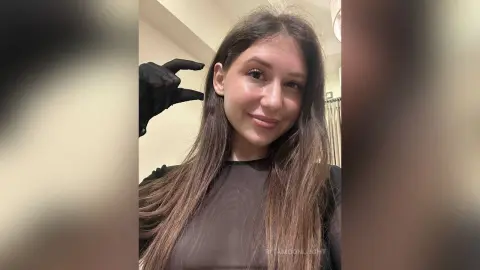 RitaMoonllight smiles while running her hand through her long brown hair, wearing a black long-sleeved top.