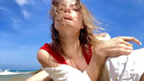 Young woman in a white summer outfit relaxing under a blue sky at a sunny beach.