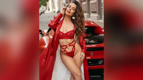 InesMoore poses in red lace lingerie and an open red coat, standing in front of a red car on a city street.