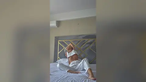 Young woman in white loungewear relaxing on a bed in a bright, modern bedroom.