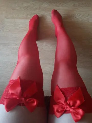 Woman wearing elegant red thigh-high stockings with large satin bows on a light wood floor.