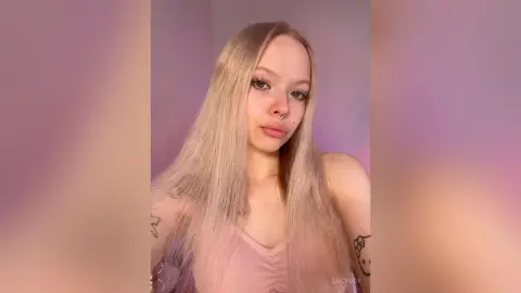 LucyLoy with long blonde hair wearing a pink tank top and looking at the camera.