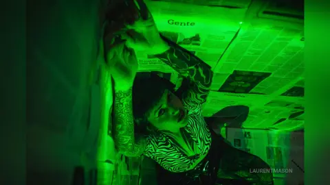 Moody portrait of a woman in a zebra print top leaning against newspaper in green neon lighting.