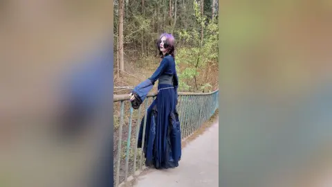 Woman in a flowing navy blue bohemian maxi dress standing on a forest path near a rustic metal railing.