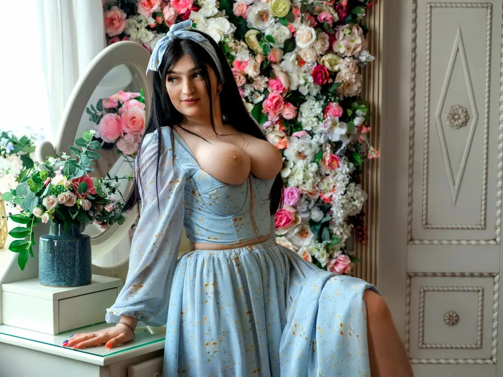Woman in light blue floral dress sitting by a floral arrangement in a bright, romantic room.