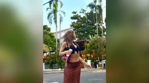 Woman in a black bikini top and leopard print skirt walking through a tropical resort setting.