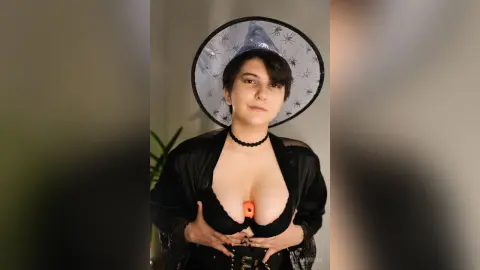 Young woman in a black witch costume and hat posing indoors with a mysterious mood.