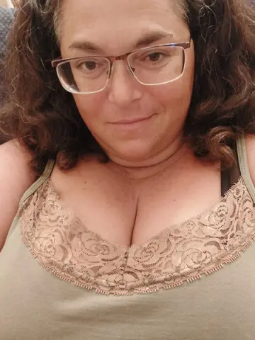 Smiling woman with glasses wearing a sage green lace camisole in a cozy indoor setting.