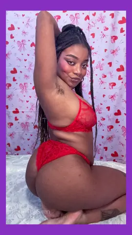 Smiling woman with long braids in red lace lingerie posing against a romantic heart pattern background.