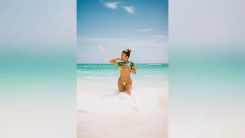 Young woman in a green bikini relaxing in turquoise ocean waves on a sunny tropical beach.