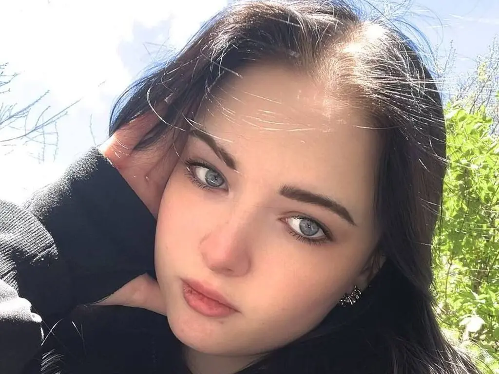 Young woman with long dark hair wearing a black sweater outdoors in bright natural sunlight.