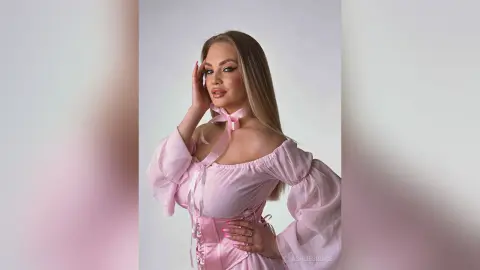 Glamorous woman in a romantic pink off-the-shoulder puff sleeve dress posing against a clean studio background.