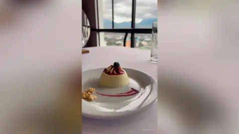 Gourmet berry cheesecake dessert served on a white plate in a luxury high-rise restaurant with a city view.
