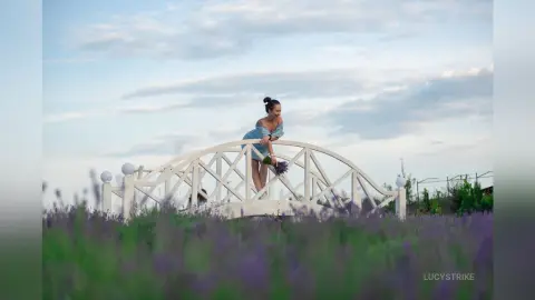 Dreamy portrait of a woman in a blue dress leaning on a white bridge amidst a blooming lavender field at dusk.