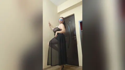 Stylish woman in a black sheer maxi dress posing confidently in a modern minimalist room.