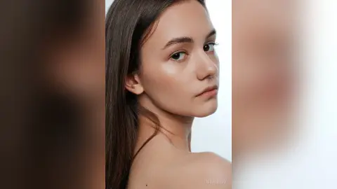 LissaDesso looks into the camera with a serious expression, showing her bare shoulders and long brown hair against a white background.