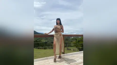 Stylish woman in a beige cutout maxi dress posing on a scenic balcony overlooking a lush green landscape.