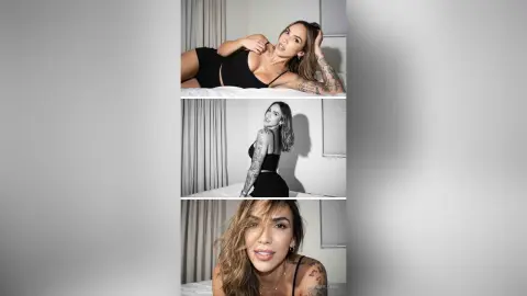 LonisMillers poses in a black top, showing her tattoos and long hair while lying on a bed.
