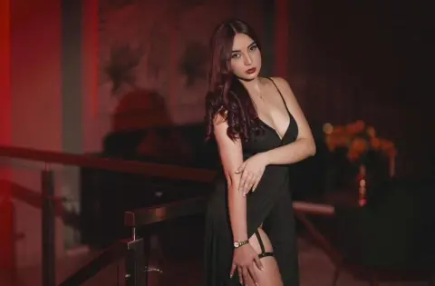 Elegant woman in a black evening dress posing in a moody, dimly lit luxury lounge setting.