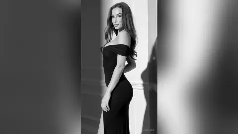Elegant woman in a black off-the-shoulder dress posing against a white pillar in a moody black and white portrait.