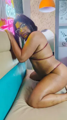 Curvy woman in minimal red lingerie relaxing on a beige sofa in a neon-lit modern room.