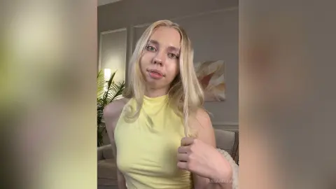 Blonde woman in a yellow halter top posing in a bright, modern living room with a serene mood.