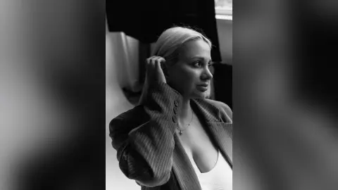 Moody black and white portrait of a blonde woman in a pinstripe blazer looking thoughtfully aside.