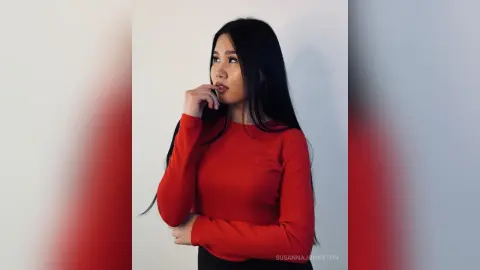 Thoughtful young woman in a long-sleeved red ribbed sweater posing against a minimalist white background.