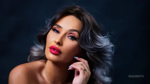 Glamorous woman with wavy hair and bold pink lipstick posing for a professional beauty portrait.