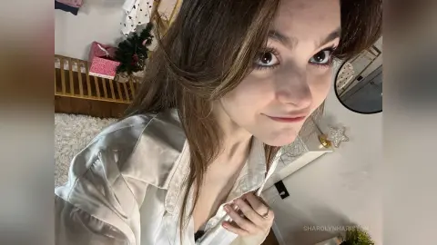 Smiling young woman with long brown hair wearing a white satin blouse in a bright indoor setting.