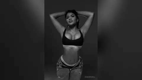 Confident young woman in black Calvin Klein sports bra and denim jeans posing in a moody black and white studio portrait.