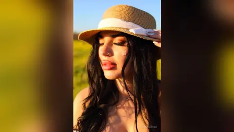 Beautiful woman in a straw sun hat posing in a golden field during a warm sunset.