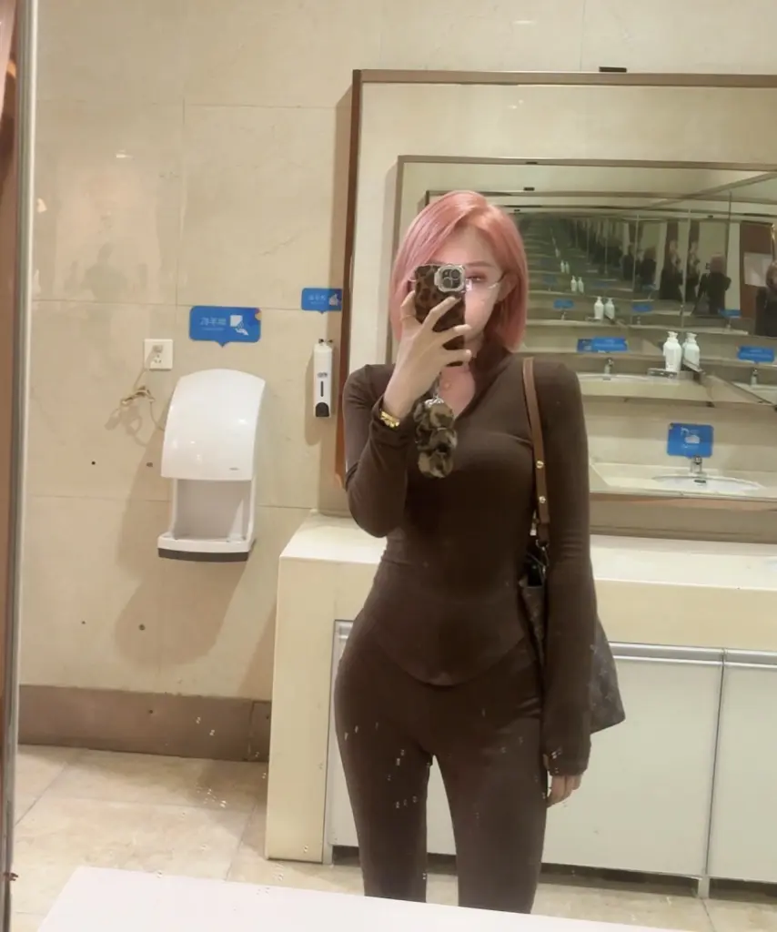 JennaLena poses for a mirror selfie wearing a red tank top, showing her long dark hair and midriff.