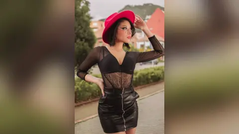 RebecaVillalobos poses outdoors wearing a red hat, a black sheer lace bodysuit, and a black leather mini skirt.