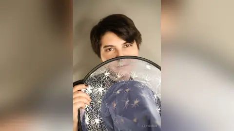 Young woman in a blue spiderweb print blouse holding a decorative patterned plate against a neutral background.