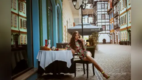 Stylish woman in a floral dress enjoying a meal at an outdoor cafe on a charming European cobblestone street.