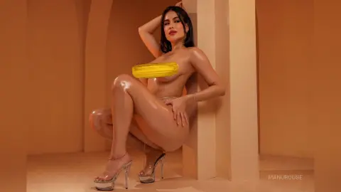 Glamorous woman in a yellow tube top and clear heels posing in a warm, minimalist studio setting.